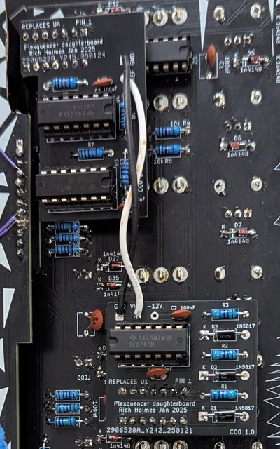 Back side of a Kosmo format synth module. Above the main circuit board are two small daughterboards connected to each other with a pair of wires. The edge of the jacks board seen above, with its bodge wires, is visible on the left.
